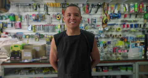 Hispanic hardware store worker smiles gently in shop aisle expressing pride appr Stock Footage 327383483