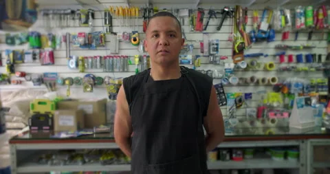 Hispanic hardware store worker standing among tools with serious expression conv Stock Footage 327383489