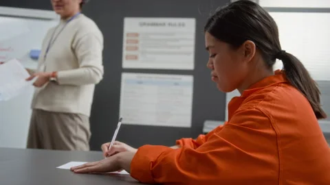 Hispanic Inmate Taking Notes Attending Class in Prison with Teacher Speaking Stock Footage 328986057