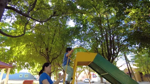 Hispanic kid playing in a playground on a slide very happy with his mother Video stock 264225333