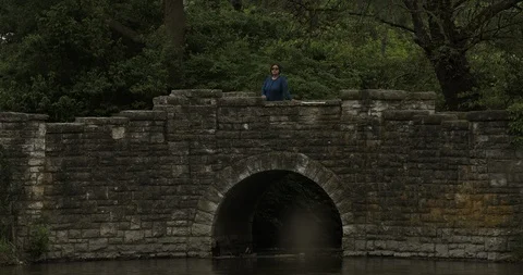 Hispanic Looks Over River From A Stone Bridge Stock Footage 108761651