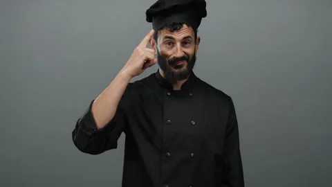 Hispanic male chef in black uniform gestures thoughtfully against grey back.. Stock Footage 313460145