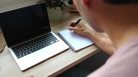Hispanic male student writing notes in notebook while teleworking at home Stock Footage 319027703