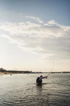 Hispanic man casting fly line off beach in afternoon Stock Photos