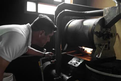 An Hispanic man is checking the burner of a coffee roaster machine Stock-Fotos