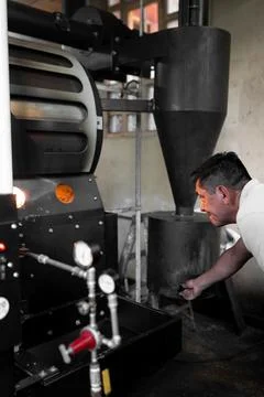 An Hispanic man is checking the burner of a coffee roaster machine Stock-Fotos