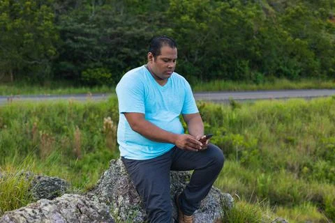 Hispanic man checking cell phone sitting on a rock Stock Photos