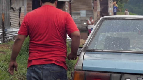 Hispanic man closing an old car door with his hip in a poor slum Stock Footage 146013754