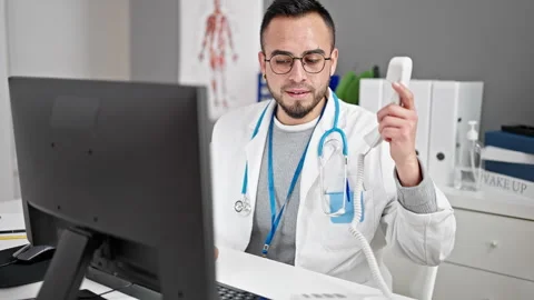 Hispanic man doctor using computer talking on telephone at the clinic Stock Footage 246143015