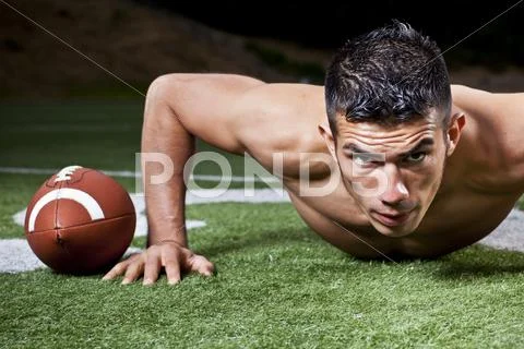 Hispanic man doing push-ups near football Stock Photos