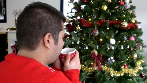 Hispanic man drinking hot beverage and looking at christmas tree decoration Stock Footage 140826808
