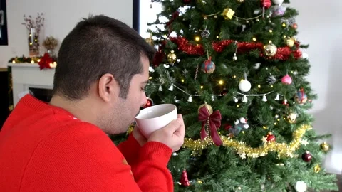 Hispanic man drinking hot beverage and looking at christmas tree decoration Stock Footage 140827976