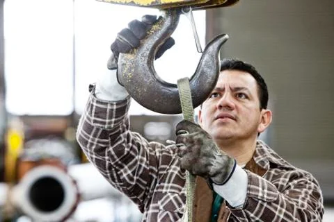 Hispanic man factory worker attaching a strap to the hook of a heavy duty Stock Photos