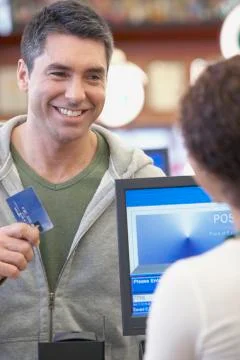 Hispanic man holding up credit card at check out Stock Photos