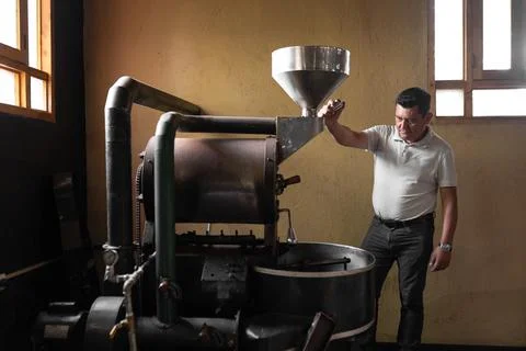 A Hispanic man is inspecting a small coffee roaster machine Stock Photos