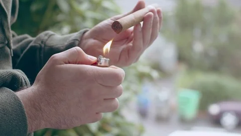 Hispanic man lighting lighter and burning end of fine cigar on front porch Stock Footage 84489977