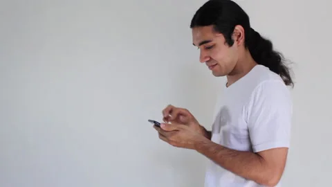 Hispanic man with long hair using a smart phone on a white background Video stock 192494314