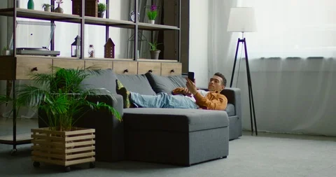 Hispanic man is lying on sofa, browsing in smartphone Stock Footage 113646996