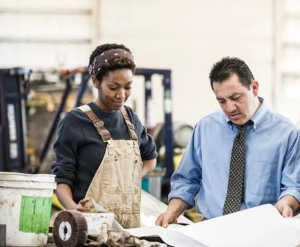 Hispanic man manager and black woman factory worker going over project plans in Fotos de archivo