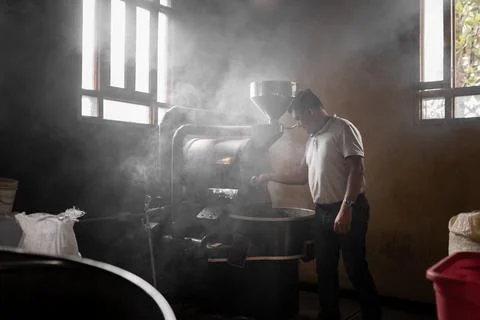 An Hispanic man is operating the roaster machine surrounded by steam Stock Photos