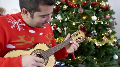 Hispanic man playing ukulele in front of a Christmas tree. Stock Footage 140870747