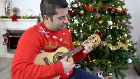 Hispanic man playing ukulele in front of a Christmas tree. Stock Footage 140875150
