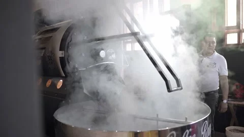 An Hispanic man is releasing coffee beans from a roaster machine with steam Stock Footage 219592640