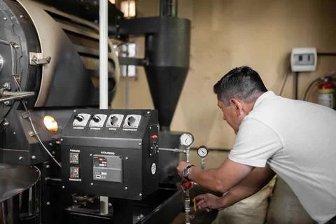 An Hispanic man is setting the buttons to turn on the coffee roaster machine Stock-Fotos