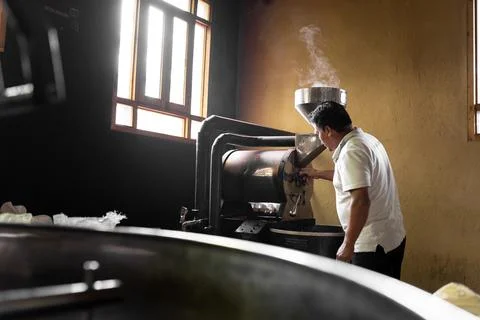 An Hispanic man is setting the controls of a coffee roaster machine Stock-Fotos