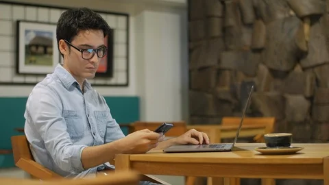 Hispanic man sitting in coffee shop using his cell phone and typing on a laptop Vídeo Stock 101716294