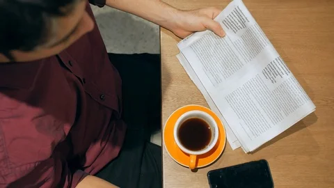 Hispanic man is sitting at table drinking coffee and reading a newspaper Vídeo Stock 101708187