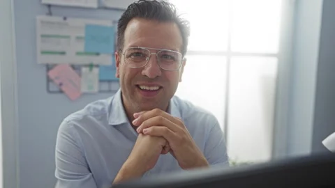 Hispanic man smiling in an office setting, hands clasped, with glasses and .. Stock Footage 280325402
