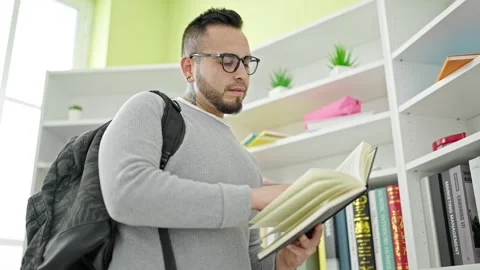 Hispanic man standing reading book at library university Stock Footage 247384334