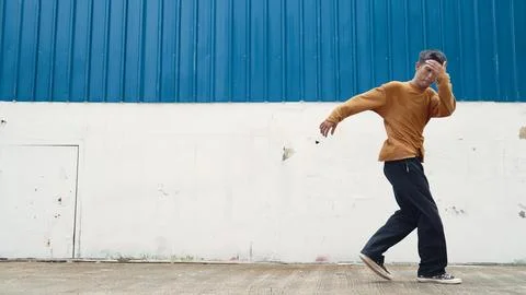Hispanic man stretch arms and dance street dancing in front of wall. Endeavor. Stock Photos
