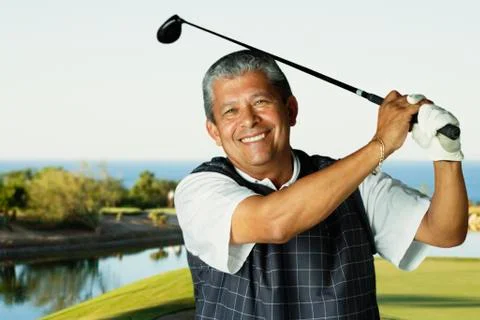 Hispanic man swinging golf club Stock Photos