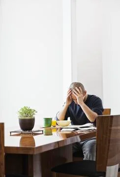 Hispanic man under stress while sitting at the dining room table in a new home. Fotos de archivo
