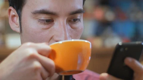 Hispanic man using cell phone and drinking a cup of coffee in a coffee shop Vídeo Stock 101704725