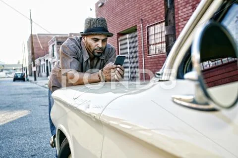 Hispanic man using cell phone on vintage car Stock Photos