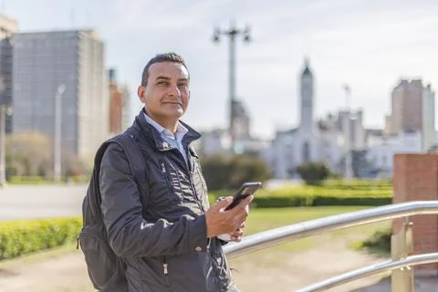 Hispanic man using his mobile phone leaning on a railing in a public park w.. Photos