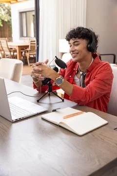 Hispanic man using usb microphone with headphones at home desk working on laptop Stock Photos
