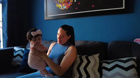 Hispanic mom happily playing with her 3 month old baby girl in the living room Stock Footage 239465613