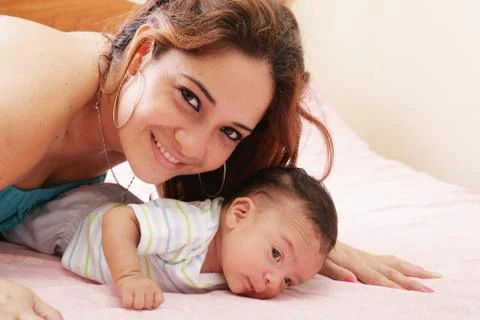 Hispanic mom lying down on bed and holding her infant son Stock Photos