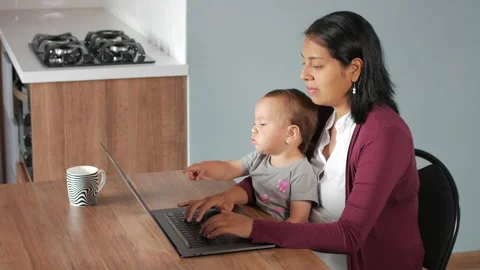 A Hispanic mother working or studying at a table with a baby girl Видео 152779211