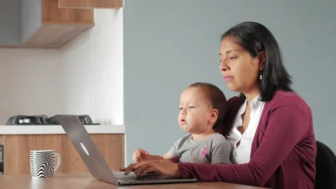 A Hispanic mother working or studying at a table with a baby girl Vídeo Stock 152779848