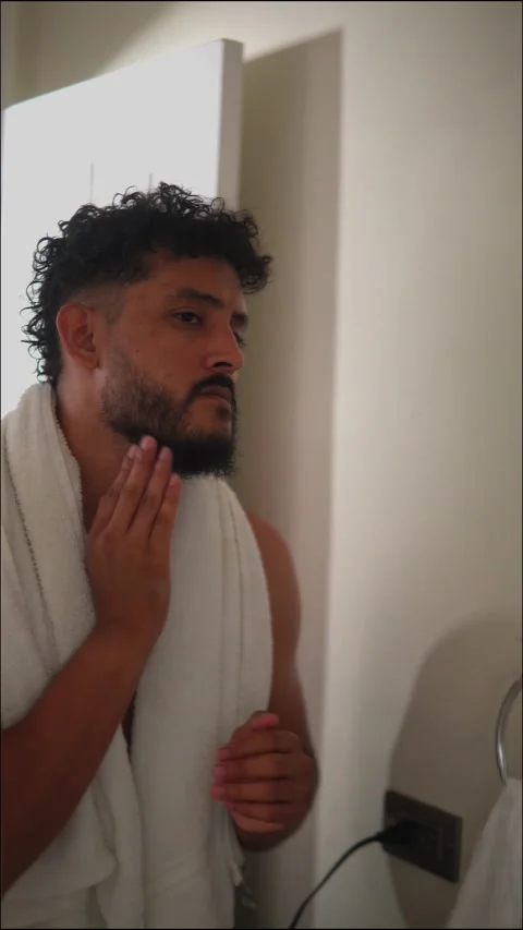 Hispanic person with beard applying aftershave in bathroom Stock Footage 336975576