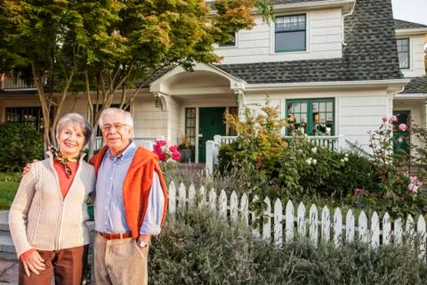 Hispanic senior couple in front of their remodeled older style home. Stock Photos