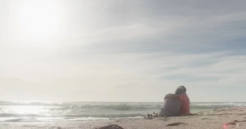 Hispanic senior couple sitting and embracing on beach at sunset Stock Footage 340978930