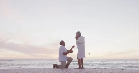 Hispanic senior man proposing to senior woman on beach at sunset Stock Footage 340007812