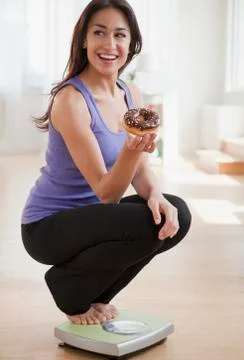 Hispanic woman holding donut and crouching on scale Stock Photos