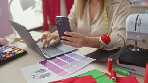 A hispanic woman multitasks in a tailoring shop using a smartphone and lapt.. Stock Footage 276173002